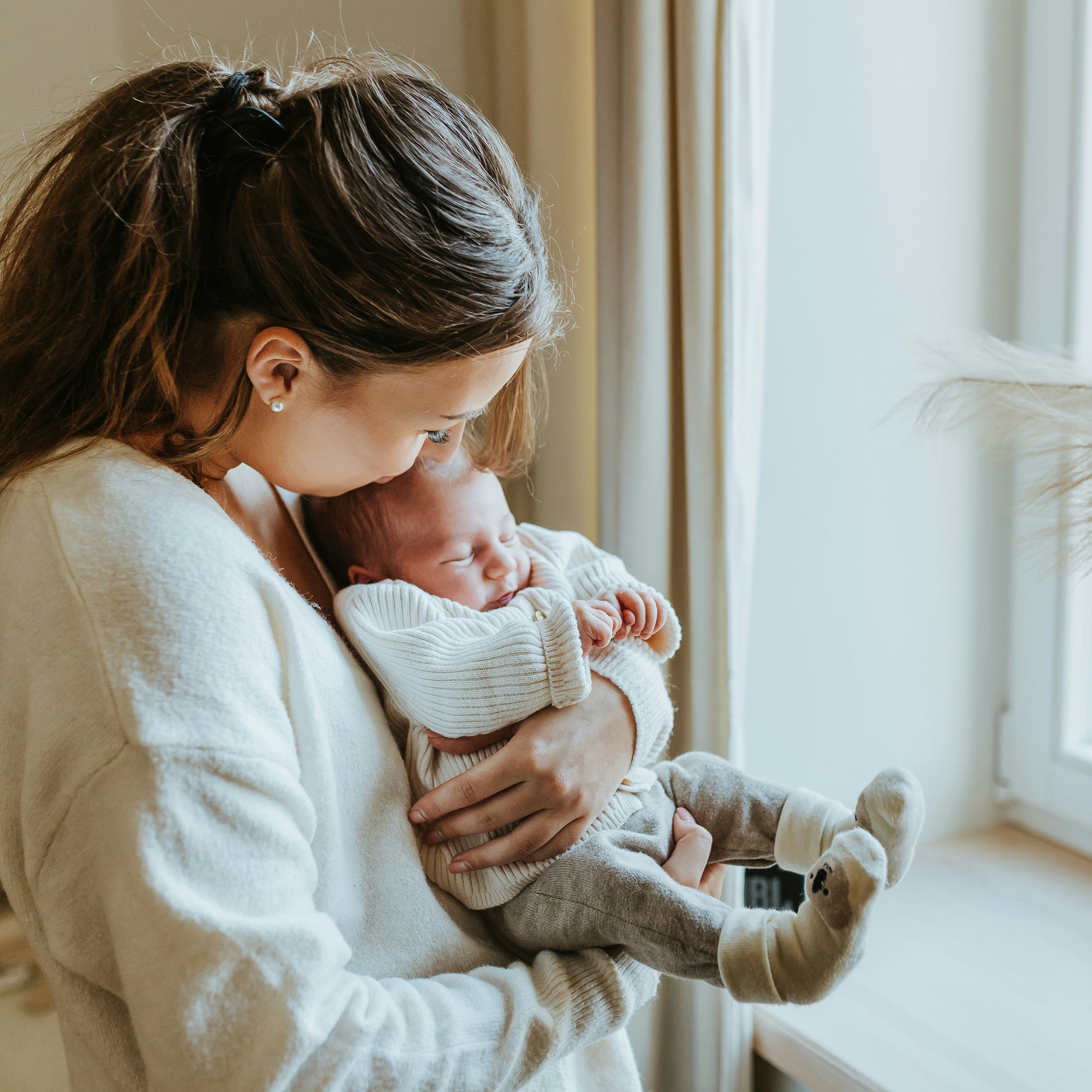Newborn care specialist gently holding a sleeping infant near natural light