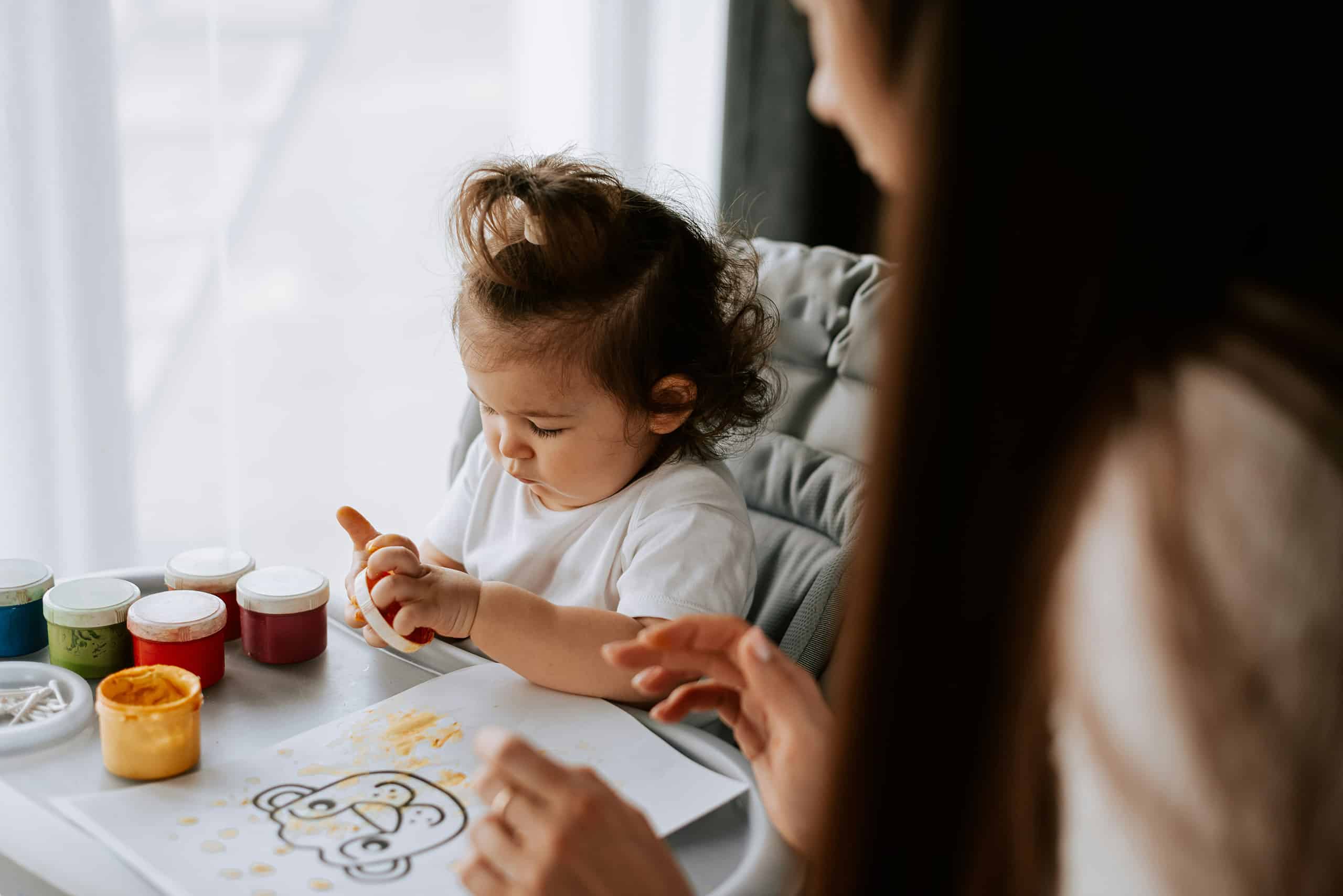Professional nanny doing creative painting and craft activities with a young toddler in a high chair