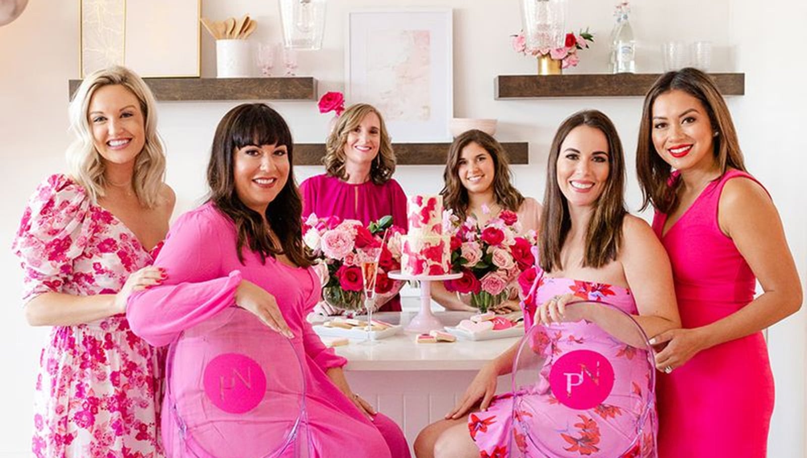 The Pink Nannies team celebrating together at a company event, dressed in pink and posing around a floral dessert table.