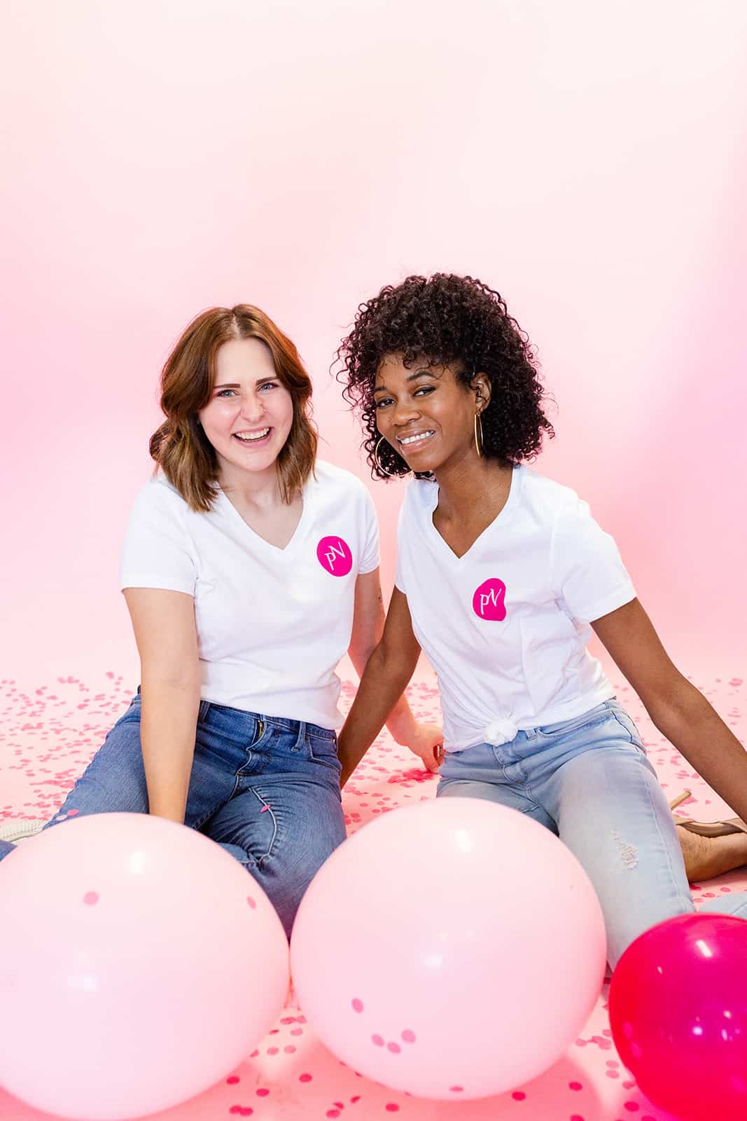 Two friendly team members smiling together sitting on the floor with pink balloons